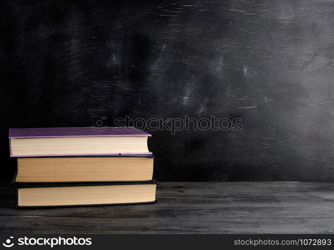 four closed books with yellow sheets on a black chalk board background, copy space, back to school concept