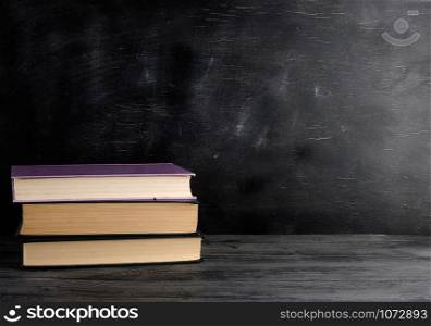four closed books with yellow sheets on a black chalk board background, copy space, back to school concept