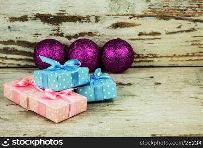 Four colored packets, Christmas presents on an old wooden table and in the background three purple, glitter baubles, shallow depth of field. Horizontal view.