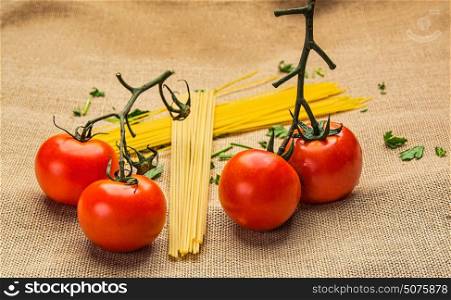 four colorful red tomatoes with green leaves and spaghetti with neutral background
