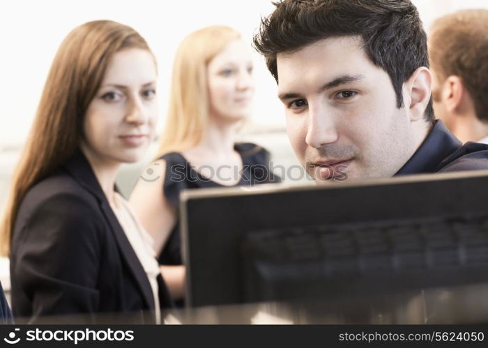 Four coworkers sitting and discussing in the office by the computer monitors