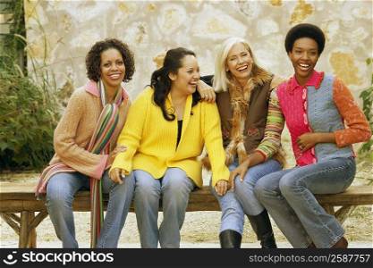 Four female friends sitting on a bench and smiling