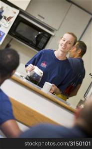 Four firefighters in break room with one getting coffee (selective focus)