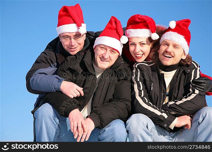 four friends against blue sky in santa claus hats