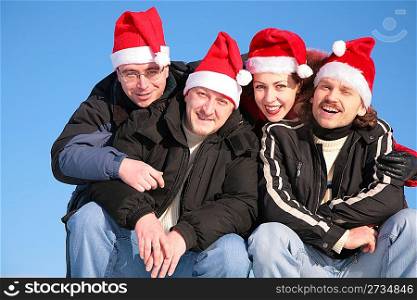 four friends against blue sky in santa claus hats