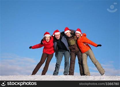four friends embracing on top of snow hill in santa claus hats