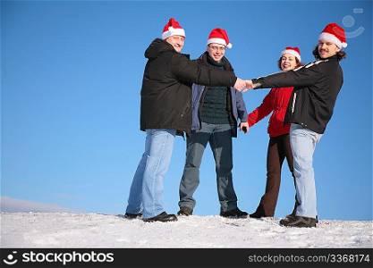 four friends hold each other for hands on snow in santa claus hats