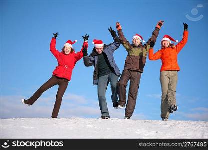 four friends jump on top of snow hill in santa claus hats