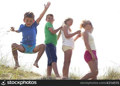 Four friends on dunes, one boy jumping, Wales, UK