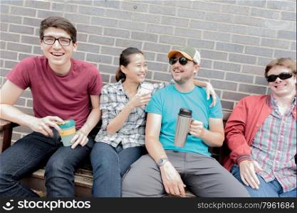 Four Friends Sat on Bench Laughing and Drinking Coffee