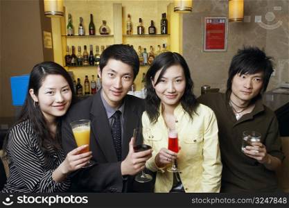 Four friends standing in front of a bar counter holding drinks in glasses