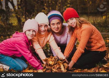 Four girls playing with autumn leaves and smiling. Girls playing with leaves