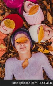 Four girls playing with autumn leaves, lying with closed eyes