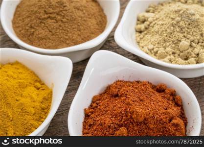 four healthy spices (turmeric, ginger, cinnamon and paprika) in white bowls