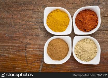 four healthy spices (turmeric, ginger, cinnamon and paprika) in white bowls on a grunge wood