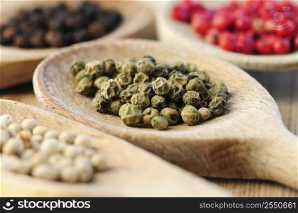 Four kinds of peppercorns in wooden cooking spoons macro