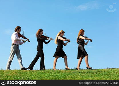 Four musicians go and playing violins against sky, side view