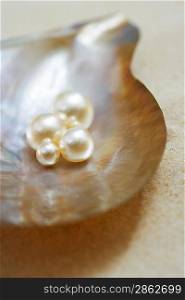 Four pearls in open oyster shell on beach close up elevated view