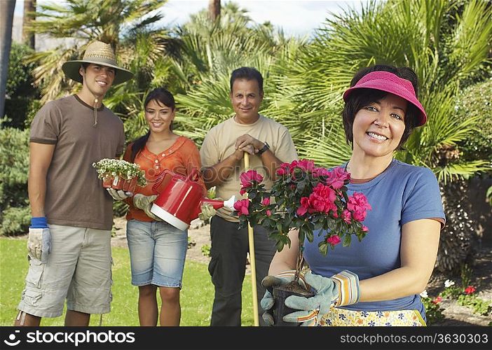 Four people gardening, focus on woman with flower in foreground