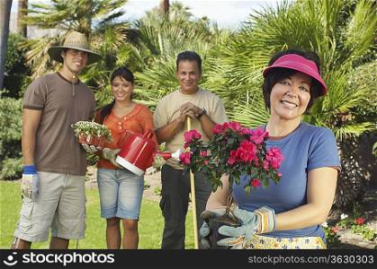 Four people gardening, focus on woman with flower in foreground