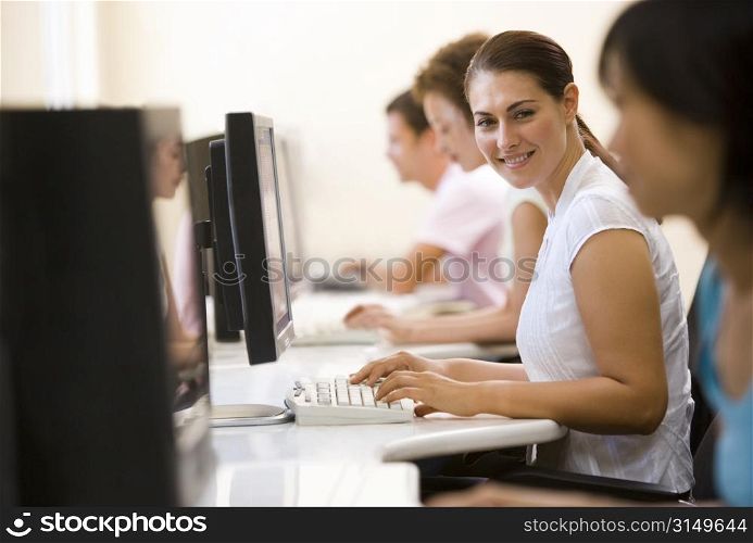 Four people sitting in computer room typing and smiling