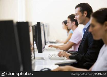 Four people sitting in computer room typing with one man in a suit