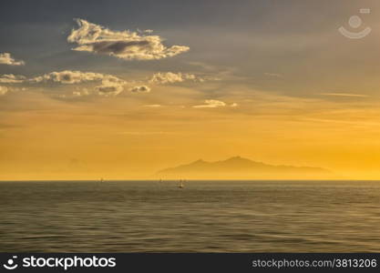 Four sailing boats in front of the island of Elba silhouetted against an orange sunrise.