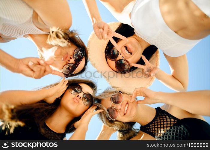 Four sexy women in sunglasses, bottom view, pool party outdoors. Beautiful girls relax at the poolside in sunny day, summer vacation. Four sexy women in sunglasses, bottom view