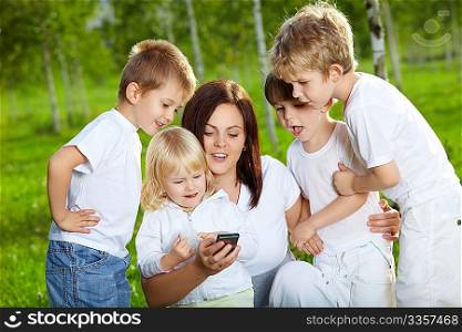 Four small child and mother are interested by a mobile phone in a summer garden