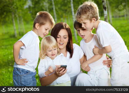 Four small child and mother are interested by a mobile phone in a summer garden