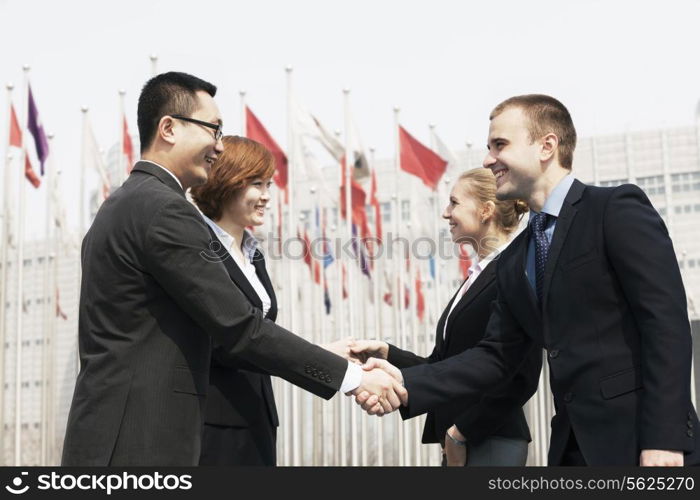 Four smiling business people meeting and shaking hands outdoors, Beijing