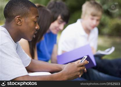 Four students outdoors studying with one checking cellular phone (depth of field)