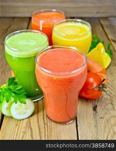 Four tall glass of tomato juice, carrot, cucumber and pumpkin, vegetables, parsley on a wooden boards background