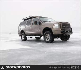 Four wheel drive truck with all terrain tires and roof rack parked on desolate frozen lake in Green Lake, Minnesota, USA.