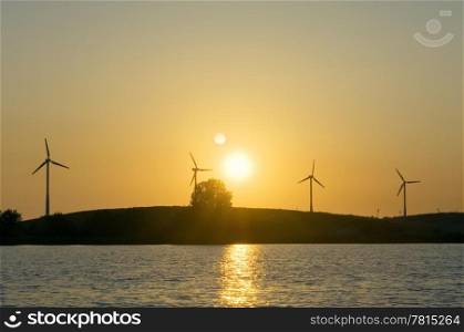 Four windmills lined up on a knoll in front of a blazing sunset