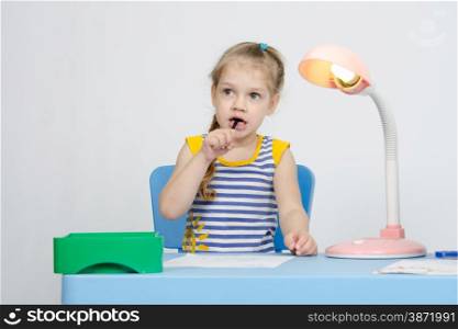 Four-year girl Europeans draws pencil on a sheet, sitting at the table