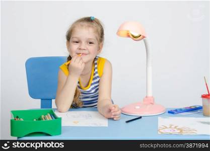 Four-year girl Europeans draws pencil on a sheet, sitting at the table