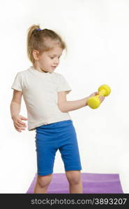 Four-year girl is engaged in raising the dumbbell exercise. Four-year girl Europeans engaged in physical exercises