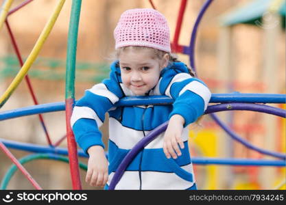 Four-year girl playing on the playground in the cool spring weather. Four-year girl provocatively wondered at the playground