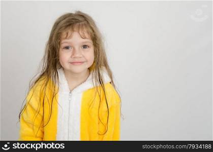 Four-year girl with wet hair in a bathrobe on a light background. Portrait of a four-year girl in bathrobe