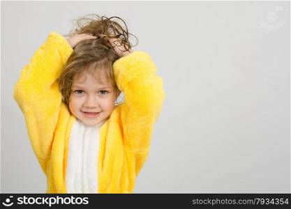 Four-year girl with wet hair in a bathrobe on a light background. Cheerful girl in yellow bathrobe holding hair