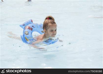 Four-year-old girl bathes in a public pool. Girl swimming on the circle. Summer day.