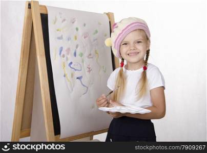 Four-year-old girl draws on the easel-painting. In the arms of children brush and palette. Light background, Studio
