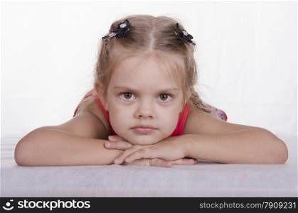 Four-year-old girl lying on his stomach, resting her head on his hands and looks into the frame. Studio light background
