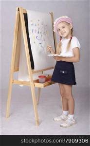 Four-year-old girl playing in the artist and draws on the easel-painting. In the arms of children brush and palette.