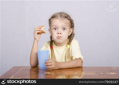 Four-year-old girl sitting at the table, eating a muffin and drinking from a plastic Cup