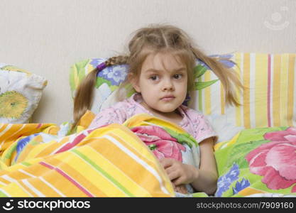 Four-year-old girl with pigtails and down the stairs. Pillow put to the wall and covered her bright blanket. Home furnishings.