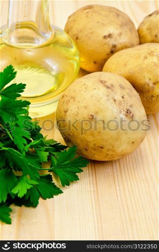 Four yellow potatoes, a bunch of parsley, vegetable oil in a bottle on the background of wooden boards