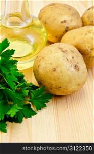 Four yellow potatoes, a bunch of parsley, vegetable oil in a bottle on the background of wooden boards