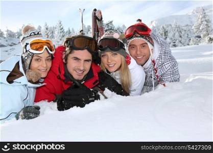 Four young adults laying in the snow